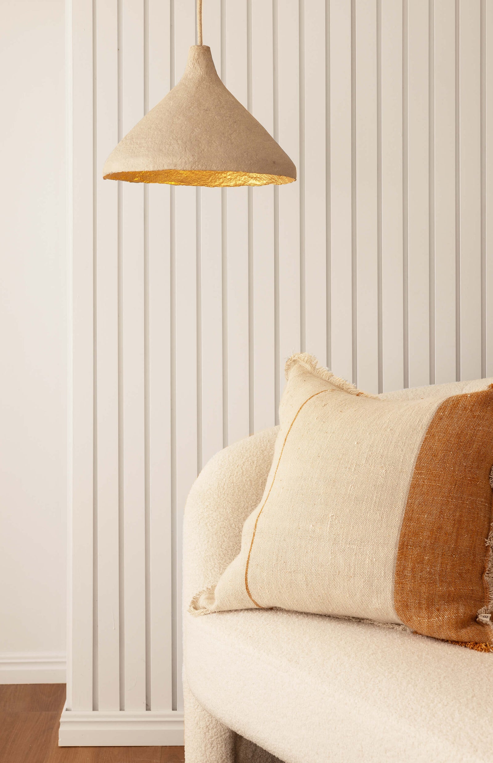 Stone coloured sustainable pendant light with gold interior hanging above a sofa