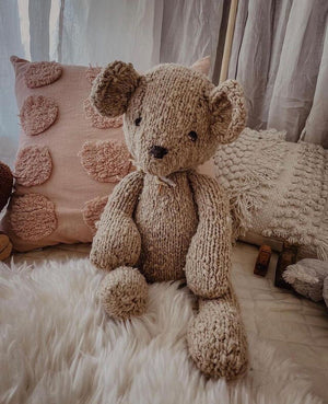 A one of a kind handmade teddy bear sits  amongst cushions