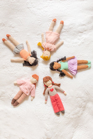 Five beautiful handmade and hand knitted woollen dolls lie on a white duvet