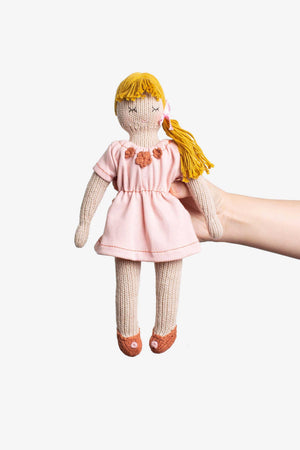 An outstretched hand holds a hand knitted doll, with yellow woollen hair and a light pink dress